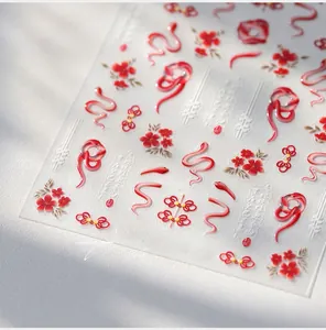 Macro shot of 3D embossed red snake and plum blossom nail stickers on a white background