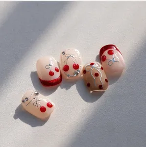 Detail of nude press-on nails featuring cherry art, silver bows, and rhinestone accents