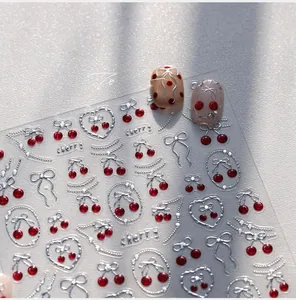 Detail of 3D embossed silver bow and red cherry nail art decals on manicured nails