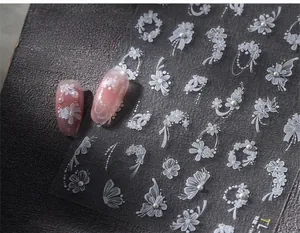 Macro shot of 3D embossed white floral nail stickers with pearls and lace on pink nails