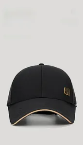 Detailed macro view of the black hard-top baseball cap featuring a golden metal logo plaque