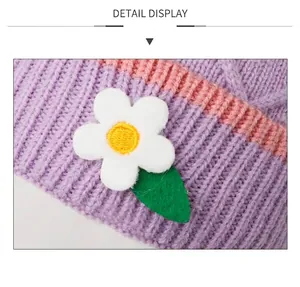 Detail van de paarse gebreide muts met roze strepen en een witte stoffen bloemdecoratie