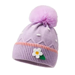 Schattige lavendel gebreide peutermuts met paarse bontpompon en kleine bloemaccent