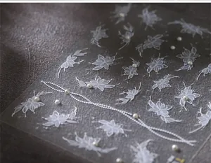 Macro detail of white lace flower nail stickers with 2mm 3D pearls on a dark background