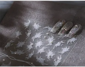 Macro shot of elegant white flower nail stickers with pearl accents on glitter nails