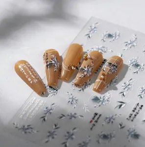 Macro detail of caramel nail art stickers featuring white flowers, gold foil, and pearls