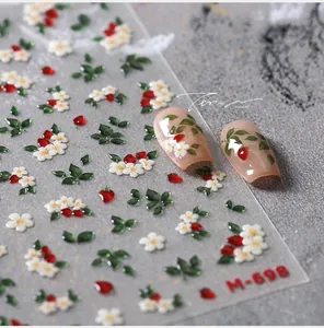 Macro shot of 3D nail art stickers featuring white flowers and red strawberry details