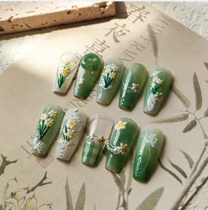 Detail of 3D embossed daisy and faux jade nail charms on dark green gradient press-on nails