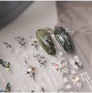Macro detail of holographic 3D butterfly and floral nail stickers on olive green nails