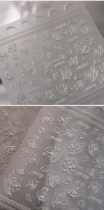 Macro detail of 3D embossed silver flower and butterfly nail art stickers with Love text