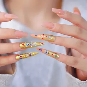 Macro shot of luxury gold stiletto press-on nails with colorful rhinestones and pearls
