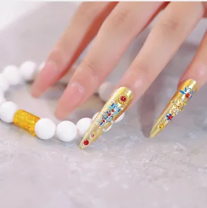 Close-up of golden hollow filigree nail guards with enamel flowers and gemstone inlays