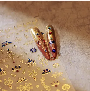 Detail of gold embossed nail stickers with blue lotus patterns on long pointed nails