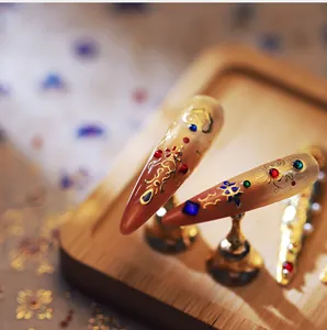 Macro view of stiletto nail art with amber tones, gold foil patterns and colorful jewels