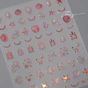 Détail macro de stickers pour ongles dorés rose avec motifs de coquillages et étoiles