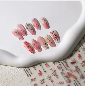 Macro detail of pink gradient press-on nails with floral motifs and gold calligraphy