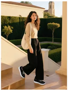 Outdoor shot of casual women sneakers with beige knit top and black wide-leg trousers