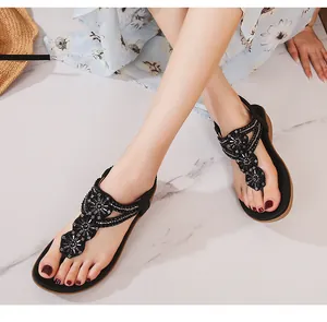 Gros plan de sandales noires aux fleurs perlées sur marbre avec robe d'été et chapeau
