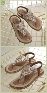 Detailaufnahme brauner flacher Sandalen mit funkelnden Strass-Blumenmustern am Riemen