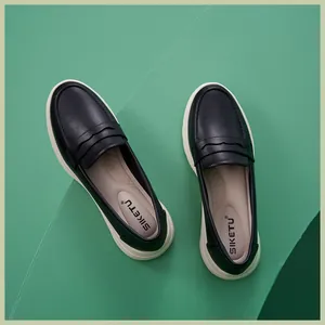 Draufsicht auf klassische schwarze Penny Loafer mit dicken weißen Sohlen auf grün