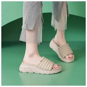 Dettaglio di sandali beige con plateau, fascia trapuntata e logo in metallo