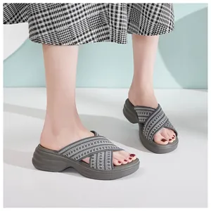 Close-up of women's wedge slides featuring grey knit crisscross straps on foot
