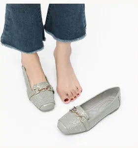 Detail van grijsgroene lakschoenen met gewatteerde stiksels en een gouden kettinggesp