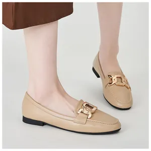 Close-up of apricot leather loafers with elegant gold interlocking chain buckles on feet