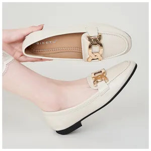 Close-up of beige loafers for women with bold gold chain buckle and black flat sole
