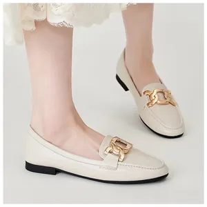 Close-up of beige leather loafers with gold chain buckle decoration on a model's feet