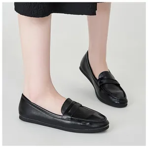 Close-up of black leather loafers worn by a model with a dark textured skirt