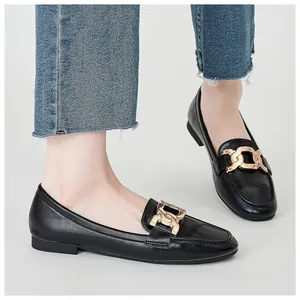 Detail of black leather loafers with gold chain buckle worn with casual blue denim jeans
