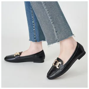 Close-up of black leather loafers with bold gold chain buckle and distressed denim pants