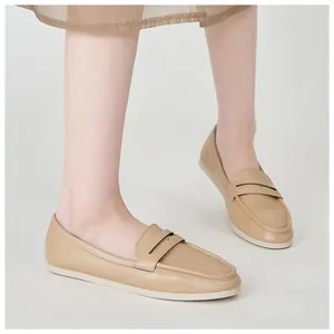 Detail view of beige leather penny loafers with round toe and flat rubber sole on feet
