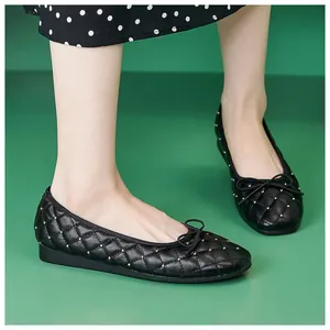 Draufsicht auf gesteppte schwarze Ballerinas mit Goldnieten und Schleife auf grünem Grund