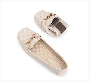 Detail van flexibele beige gewatteerde loafers met een decoratieve gouden kettinggesp