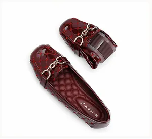 Detailopname van flexibele bordeauxrode laklederen loafers met ruitpatroon en ketting