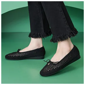 Close-up of black hollow mesh ballet flats with bow detail paired with frayed denim jeans
