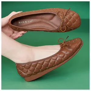 Detail brauner gesteppter Ballerinas mit Goldnieten und Schleife auf grünem Grund