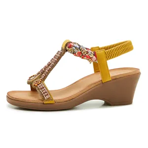 Détail de sandales compensées jaunes avec perles T-strap et nœud en tissu floral