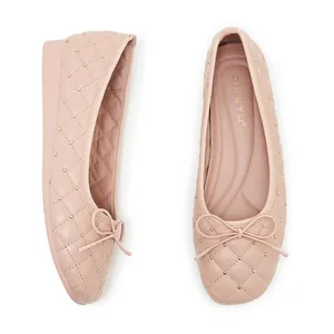 Detail von nudefarbenen gesteppten flachen Schuhen mit Goldnieten und zarter Schleife