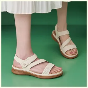 Side view of cream-colored cross-strap sandals with perforated details on model's feet