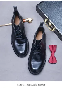 Classic black leather boots with laces and heel pull tab displayed on a grey vintage suitcase