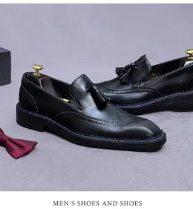 Détail de chaussures brogues en cuir noir avec glands et gravure d'ailes sur fond gris
