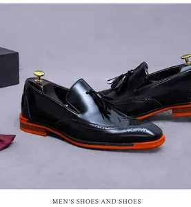 Dettaglio di mocassini da uomo in pelle nera con ricamo brogue e suola arancione