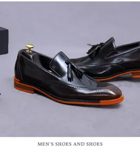 Dettaglio di mocassini brogue marroni da uomo con suola arancione e nappe doppie