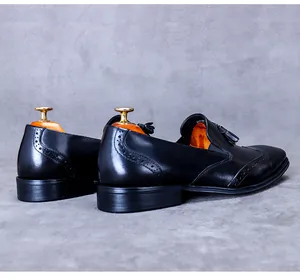 Detail view of black leather oxfords with brogue carving and tassels on a grey background