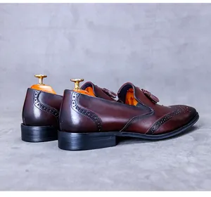 Detail of reddish brown gradient leather loafers featuring fringe and brogue perforations