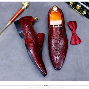 Deep red crocodile embossed leather loafers with luxury accessories on grey surface