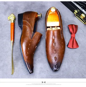 Draufsicht auf braune Leder-Loafer mit Krokodilprägung, inklusive Schuhanzieher und Fliege